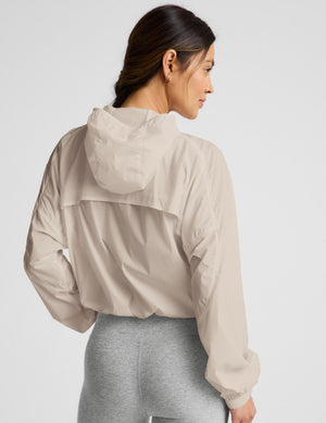 Woman wearing a beige jacket and gray pedal pushers against a plain background. 