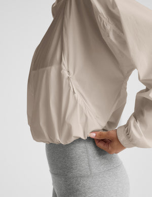 Woman wearing a beige jacket and gray pedal pushers against a plain background. 