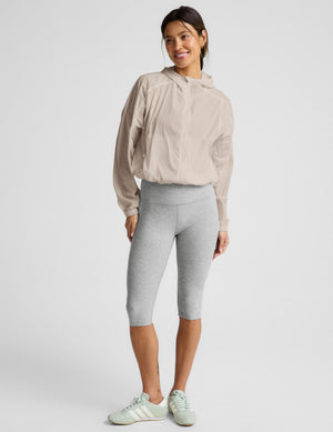 Woman wearing a beige jacket and gray pedal pushers against a plain background. 