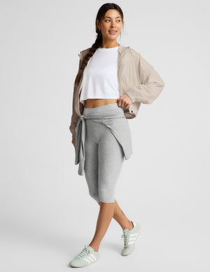Woman wearing a beige jacket and gray pedal pushers against a plain background. 