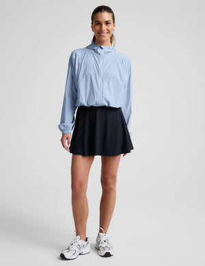 Woman wearing a light blue jacket and navy blue skirt against a plain background.