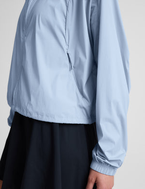 Woman wearing a light blue jacket and navy blue skirt against a plain background.