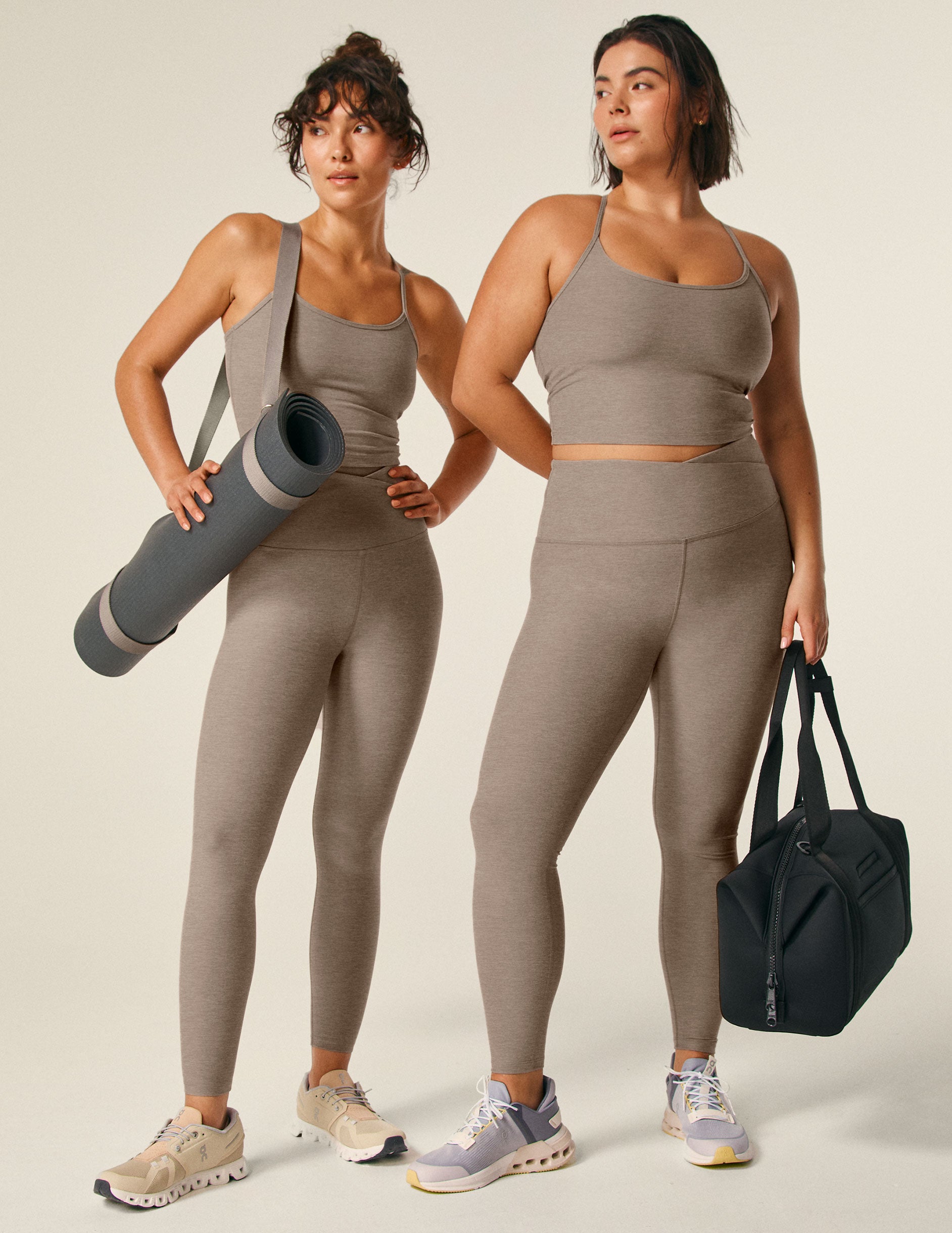 model is wearing a brown cropped racerback tank top and brown high-waisted midi leggings with a front crossover detail. 