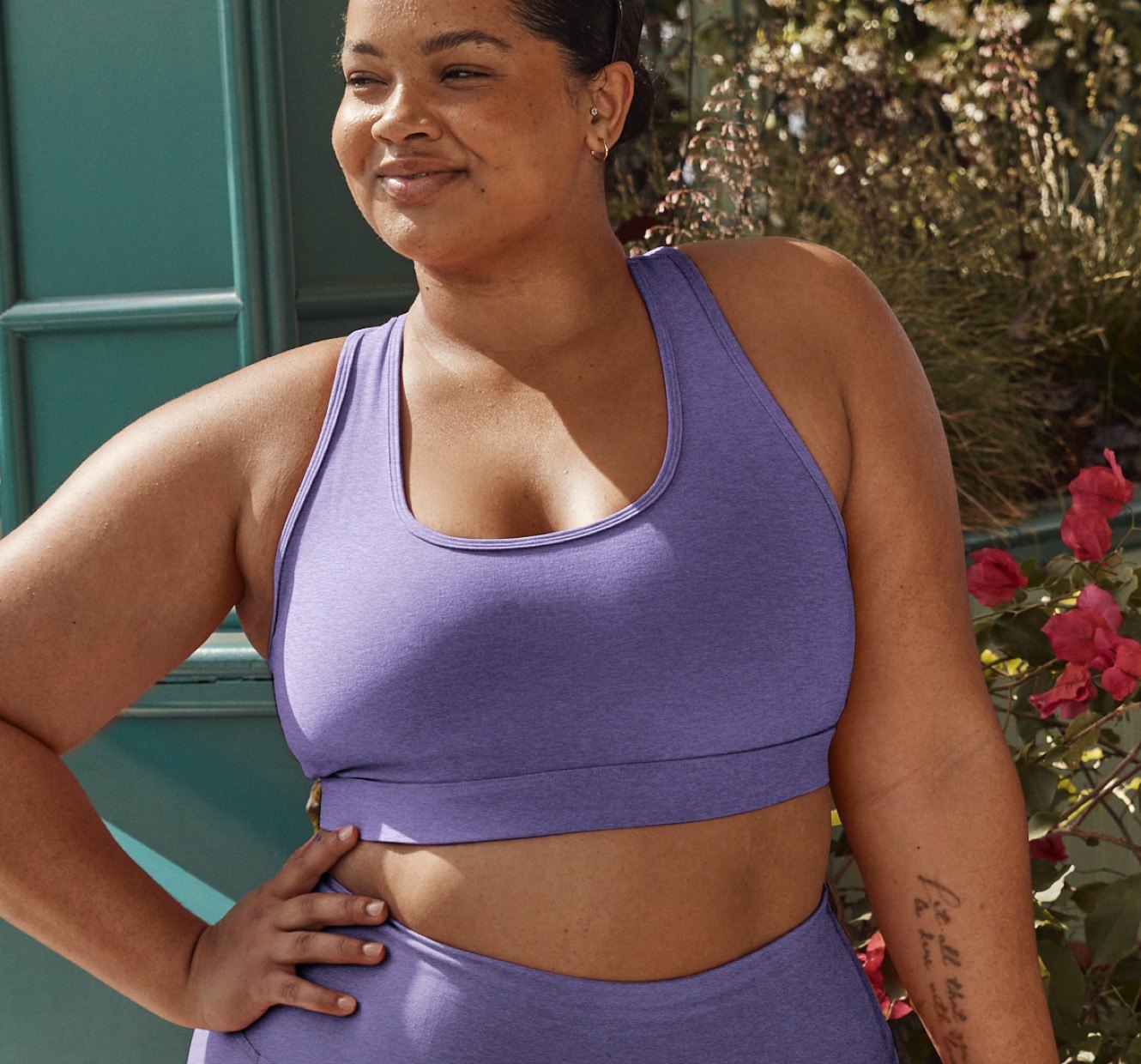 model is wearing a purple bra top and purple high-waisted midi leggings. 