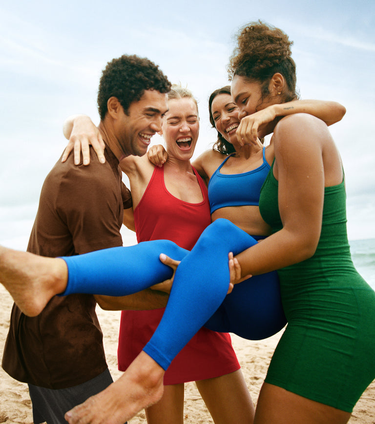 model on left is wearing a brown men's t-shirt. model on center left is wearing a red halter tank dress. model on center right is wearing a blue bra and blue high-waisted midi leggings. model on far right is wearing a green tank and green high-waisted biker shorts.