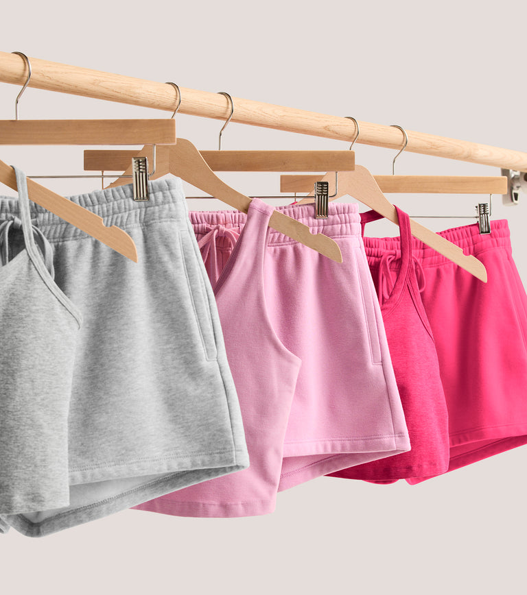 hanging flatlay of grey fleece shorts, pink fleece shorts, and hot pink fleece shorts.