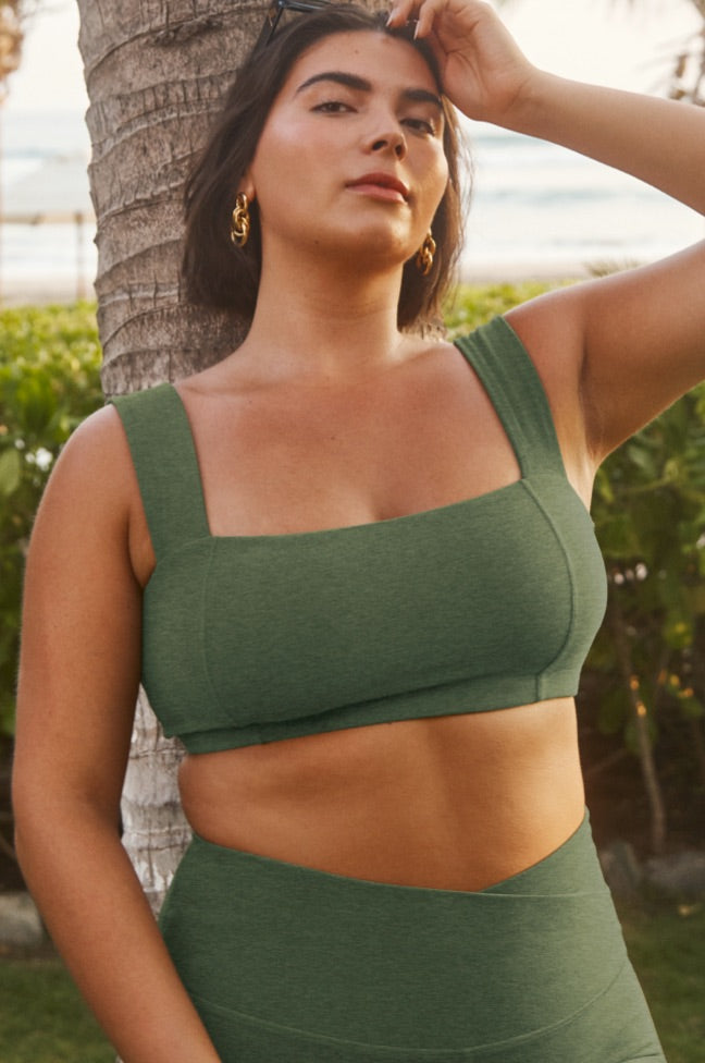 model is wearing a green squared bra top and green high-waisted midi legging with a front crossover detail on the waistband. 