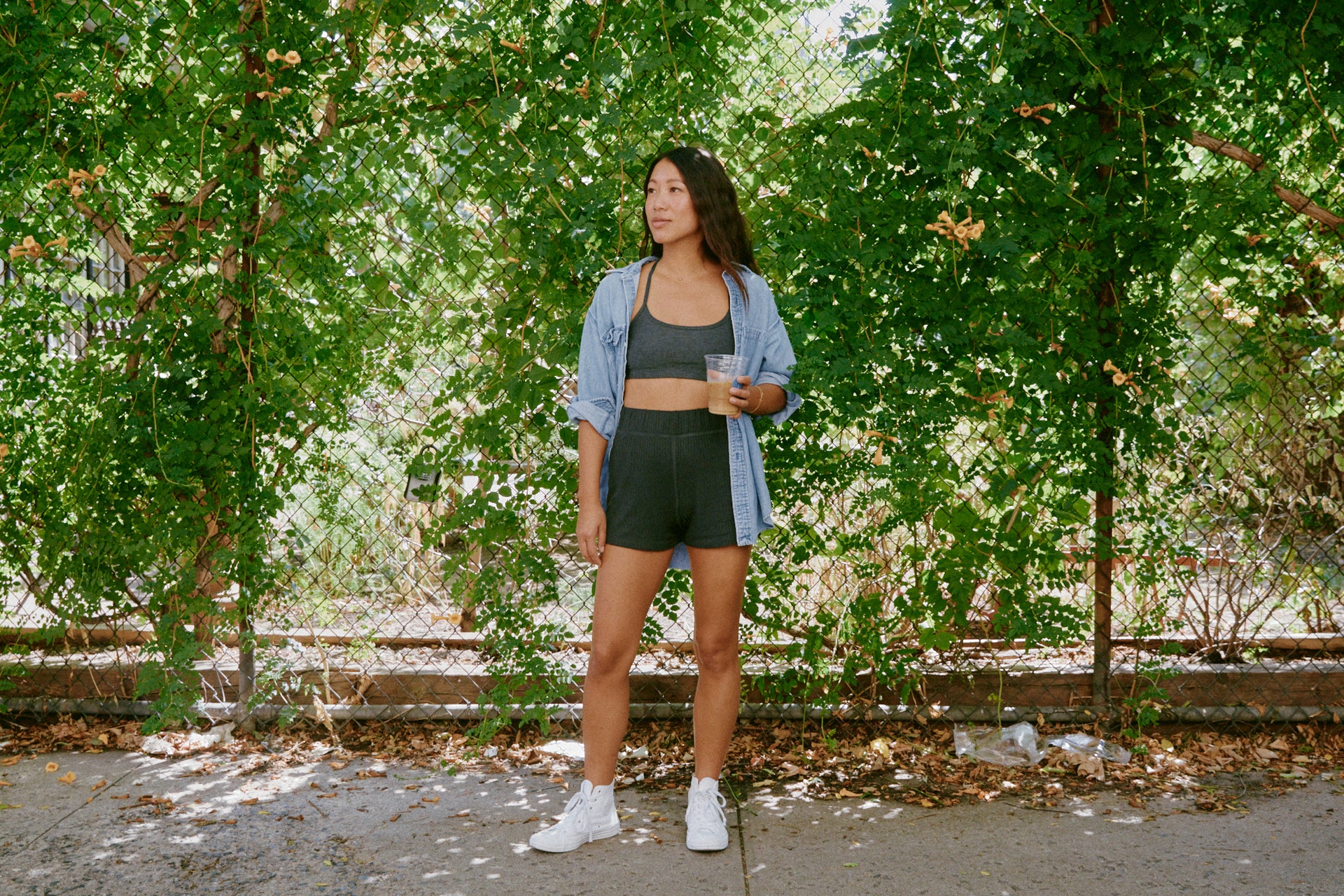 Claire standing outside against a fence and holding a coffee