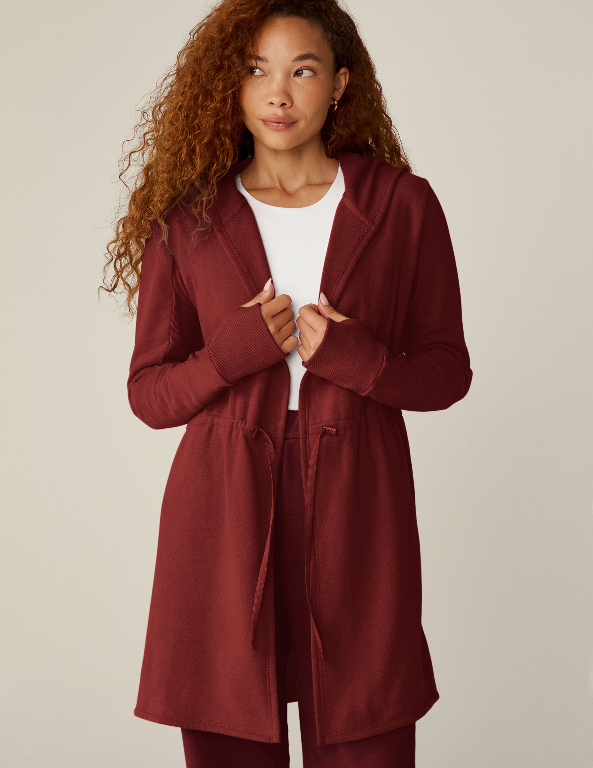 red long length hooded jacket with a drawstring at the waist and side pockets.