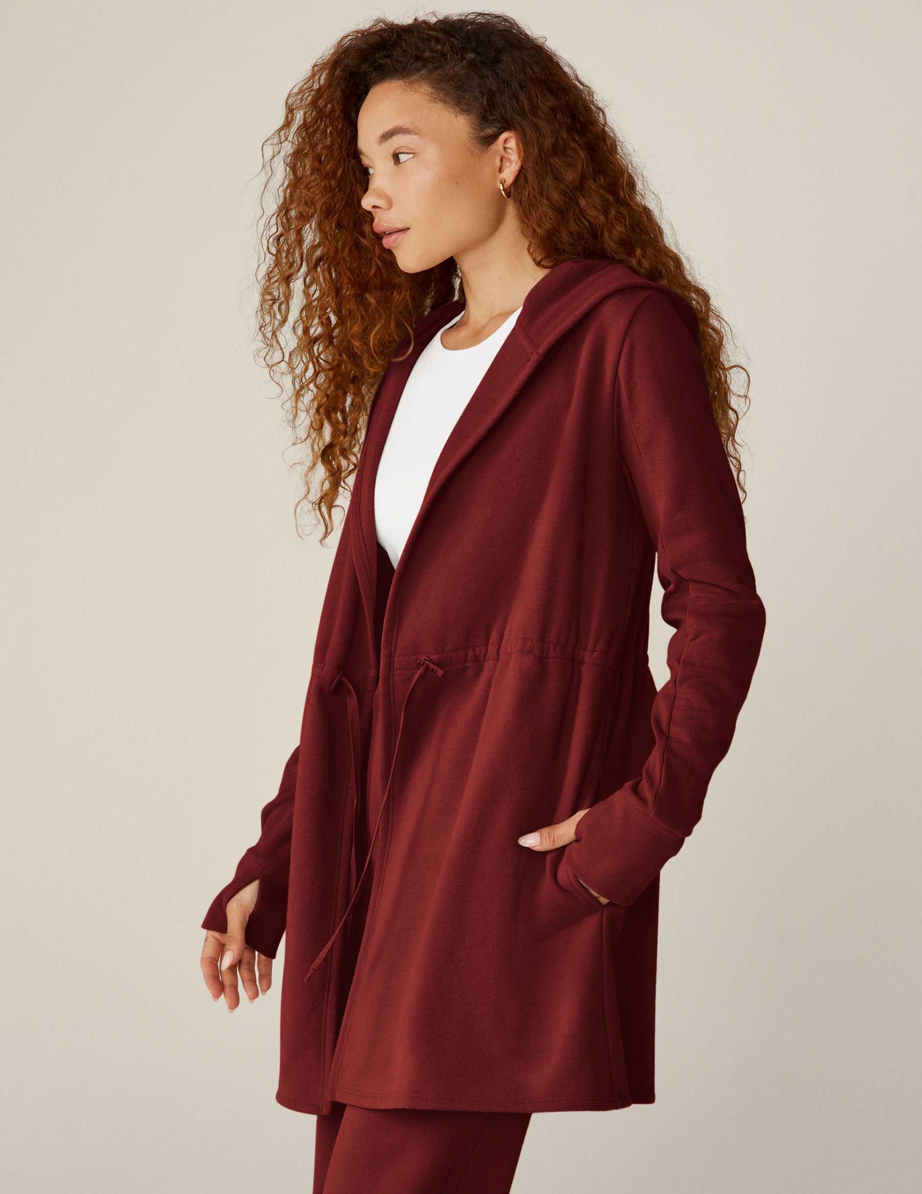 red long length hooded jacket with a drawstring at the waist and side pockets.