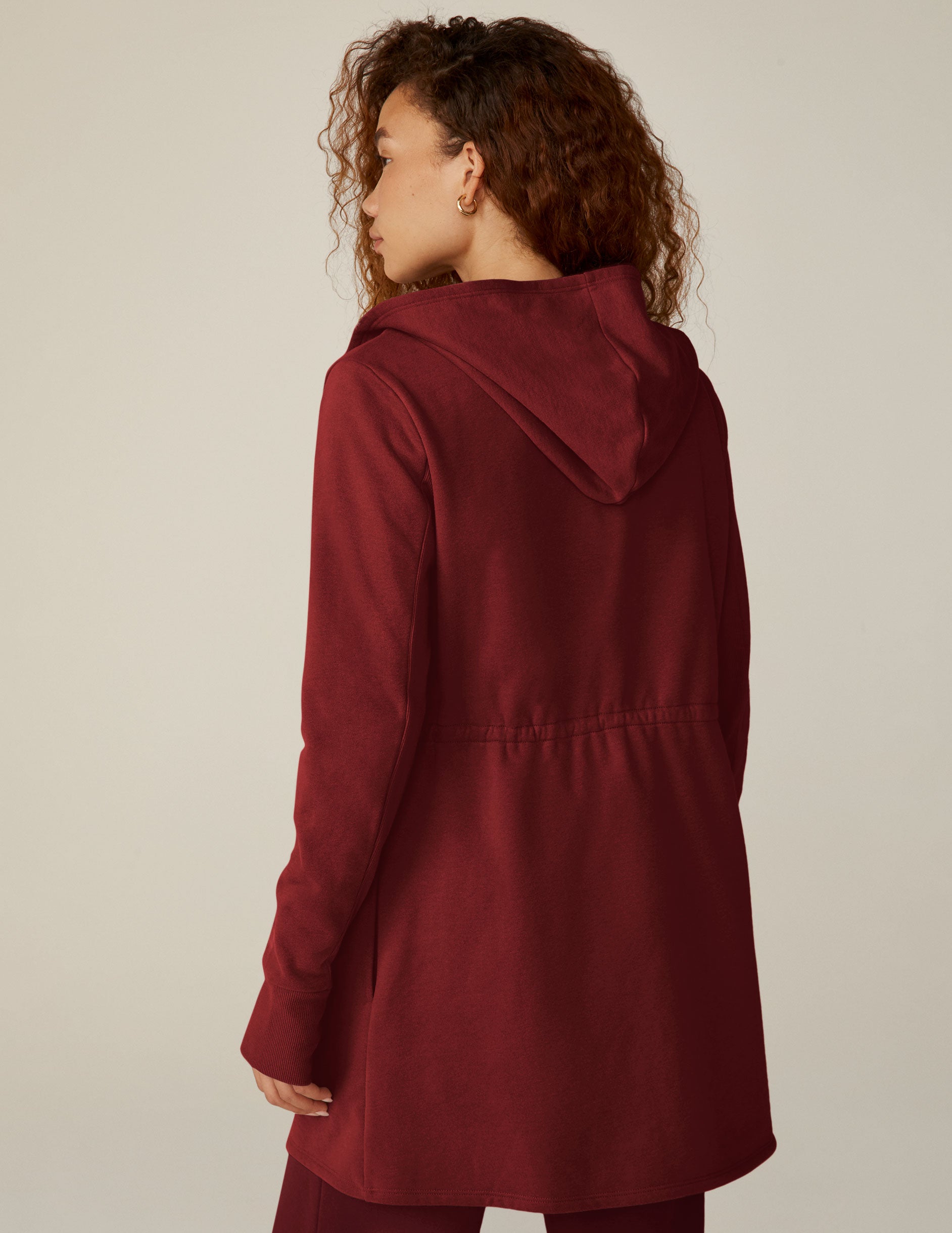 red long length hooded jacket with a drawstring at the waist and side pockets.