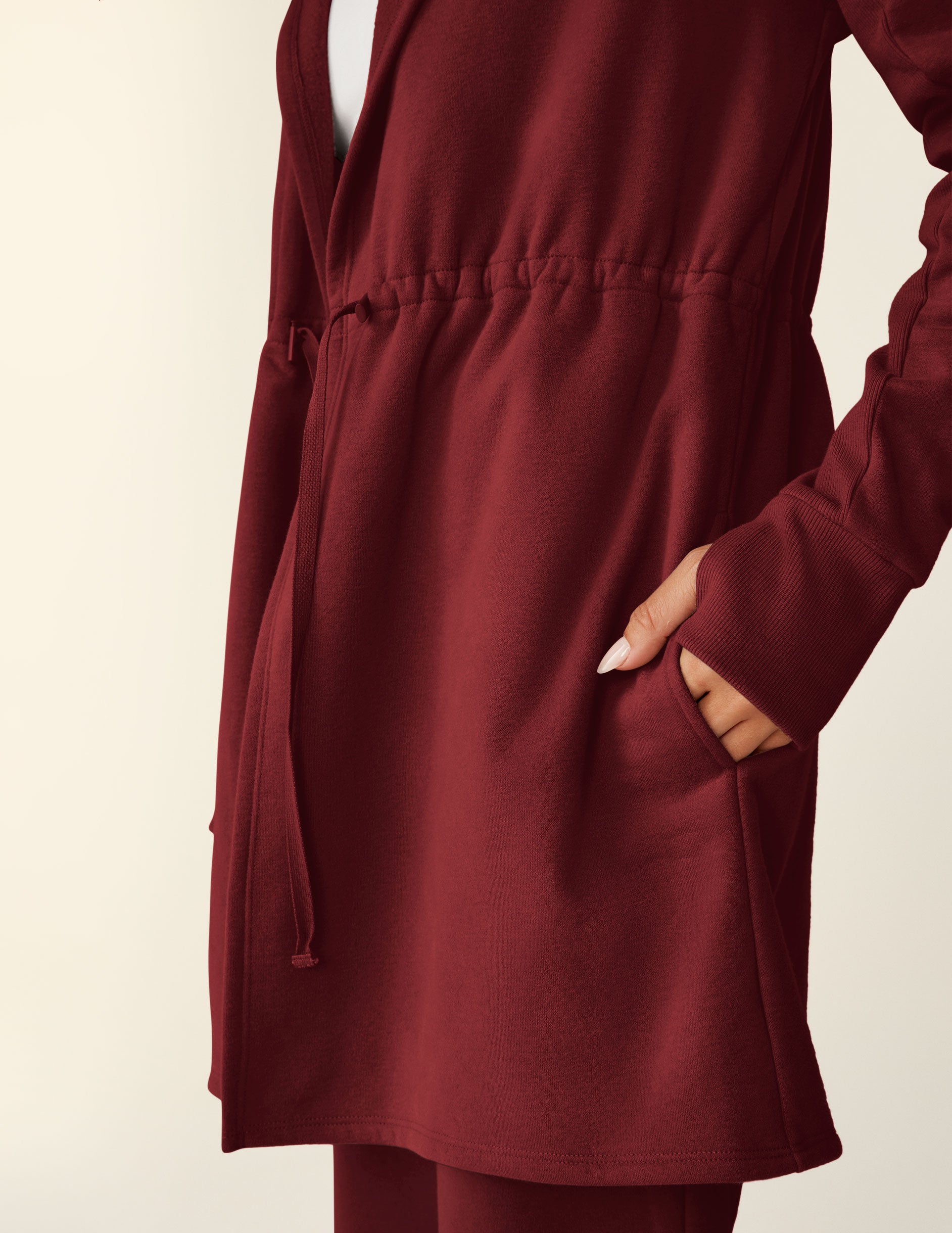 red long length hooded jacket with a drawstring at the waist and side pockets.