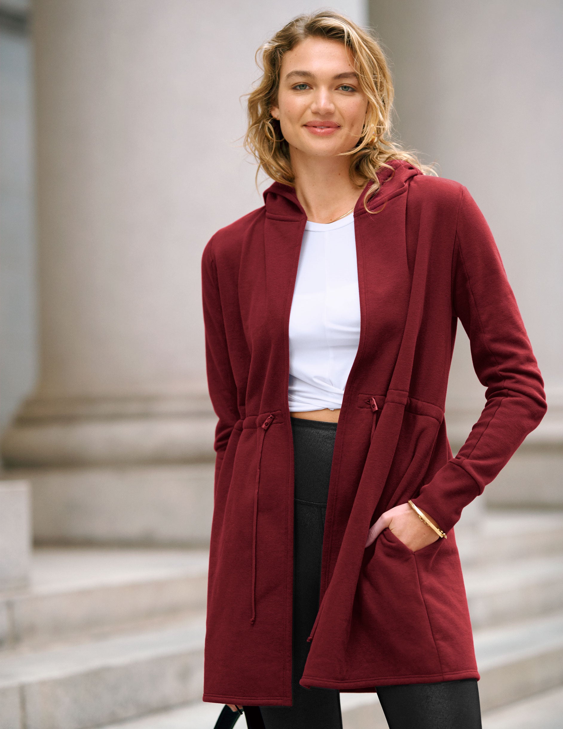 red long length hooded jacket with a drawstring at the waist and side pockets.