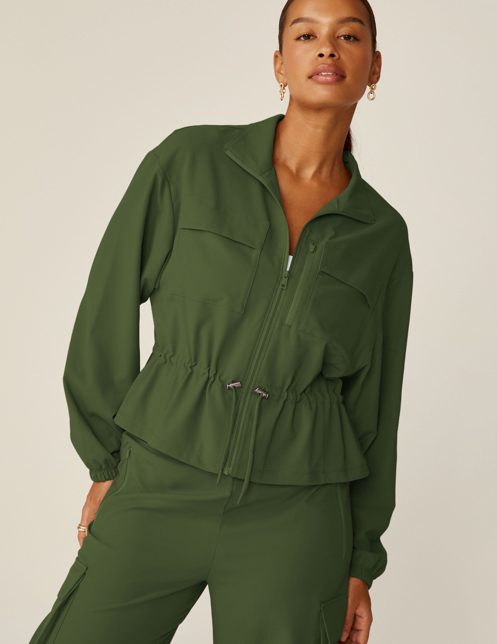 green zip-up jacket with a drawstring at waistband and cargo style pockets.