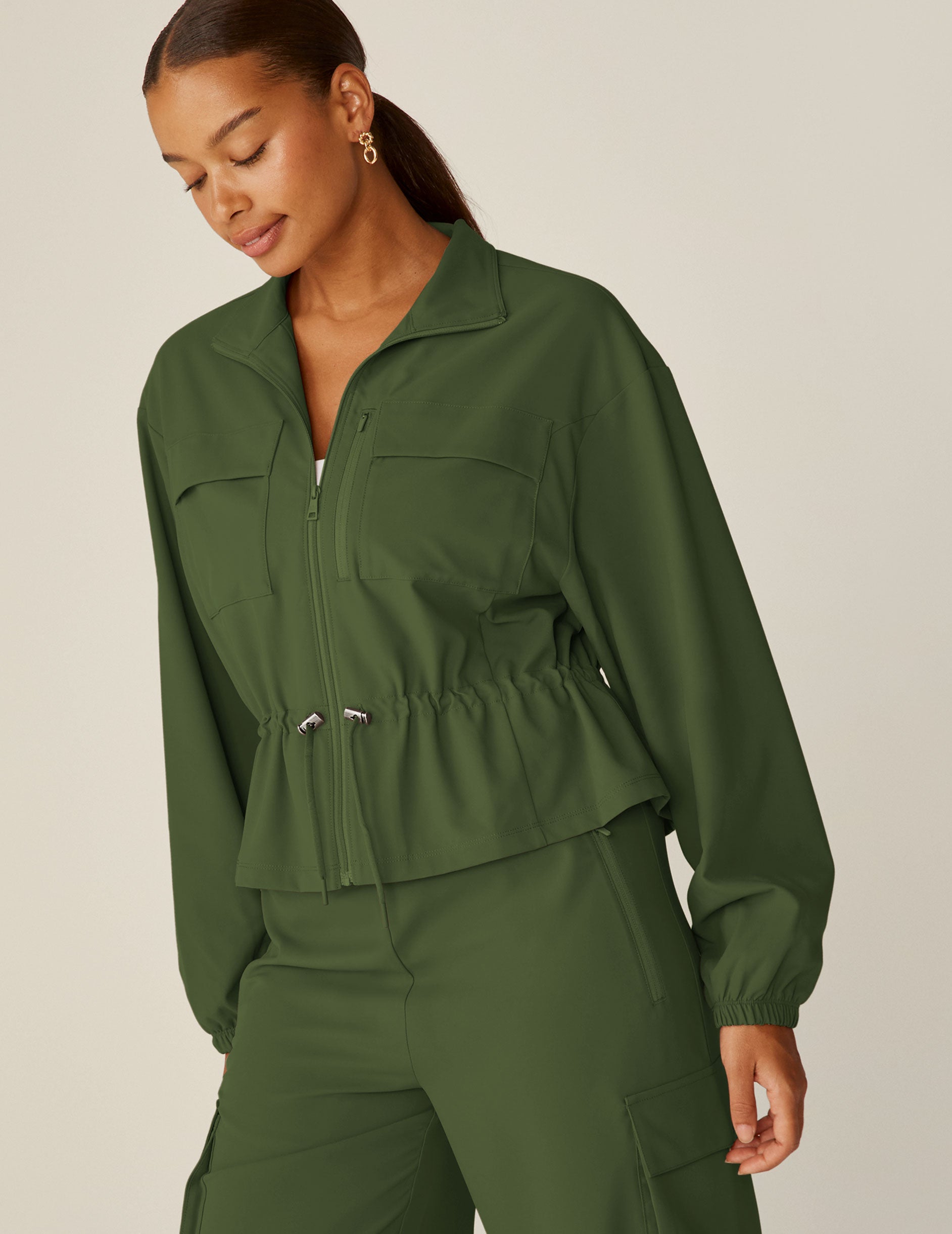 green zip-up jacket with a drawstring at waistband and cargo style pockets.