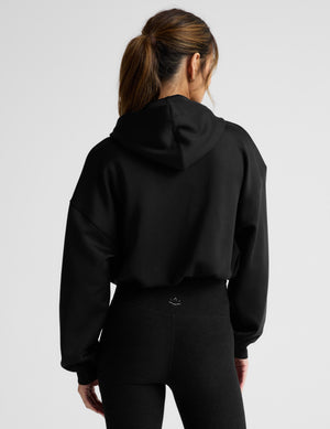 Person wearing a black hoodie and black pants on a light gray background. 