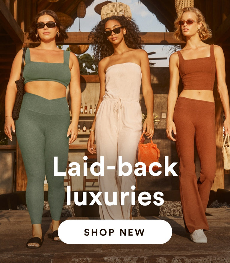 model on the right is wearing a green square neck bra top and green high-waisted midi leggings. model in the center is wearing a white terry fabric jumpsuit model on the left is wearing an orange square neck cropped tank and orange low-waisted flare leggings.  