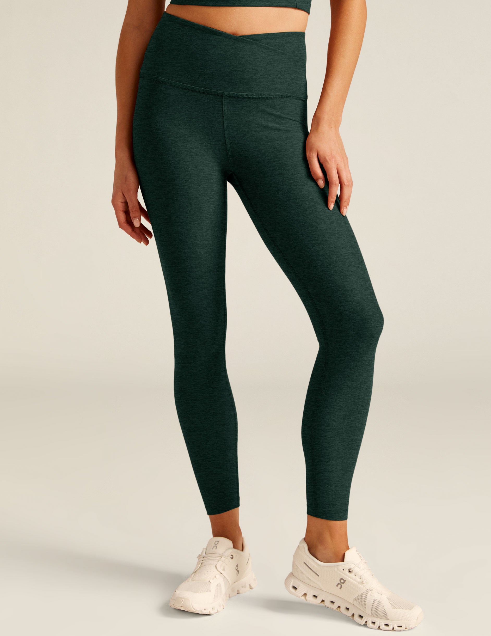 green high-waisted midi leggings with a crossover design on the front waistband. 