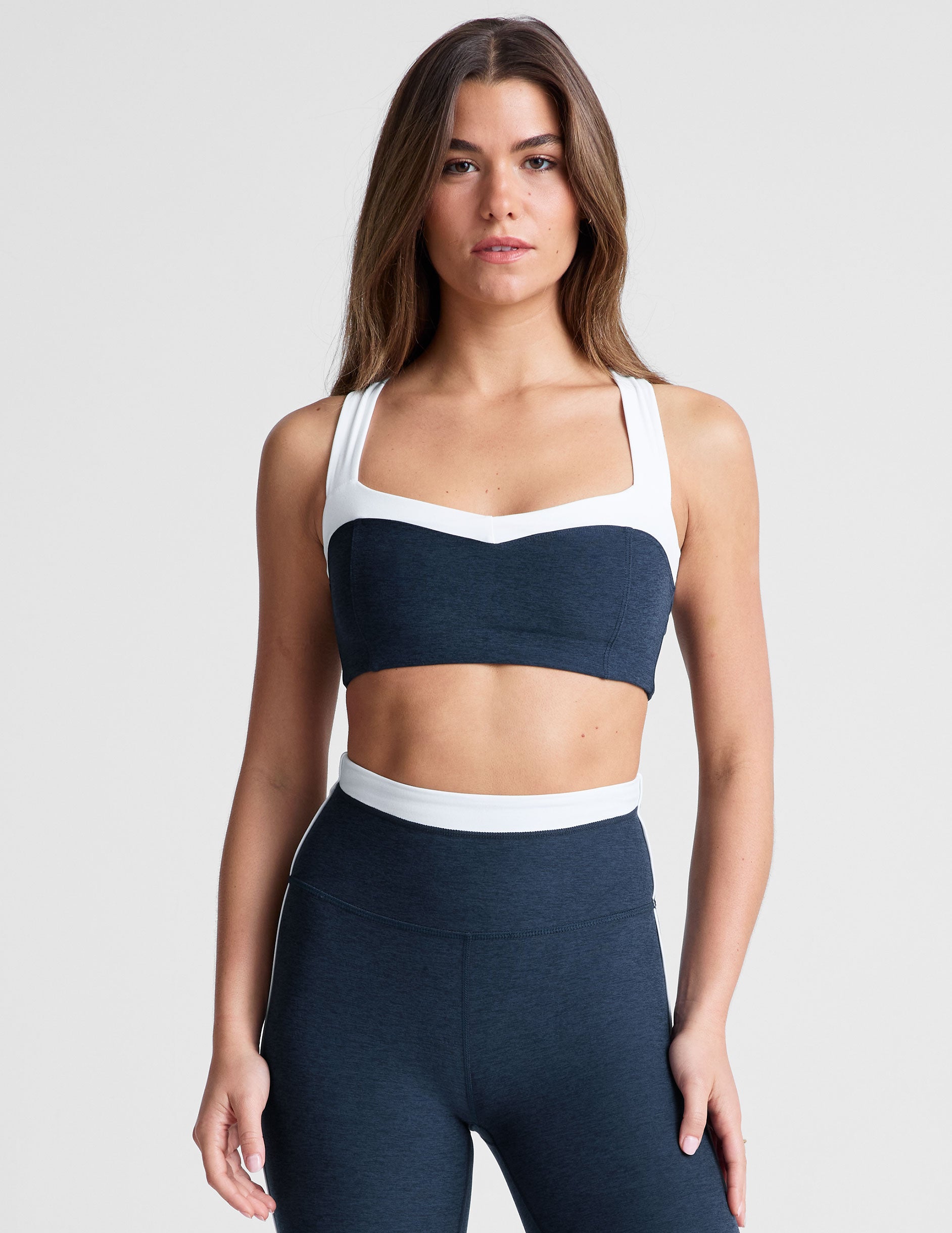 navy blue self-lined, medium to low support bra top with a colorblock sweetheart neckline panel, contrast straps, and princess seams. bra is paired with navy blue high-waisted midi leggings with a white contrast trim around waistband and down sides of legs.