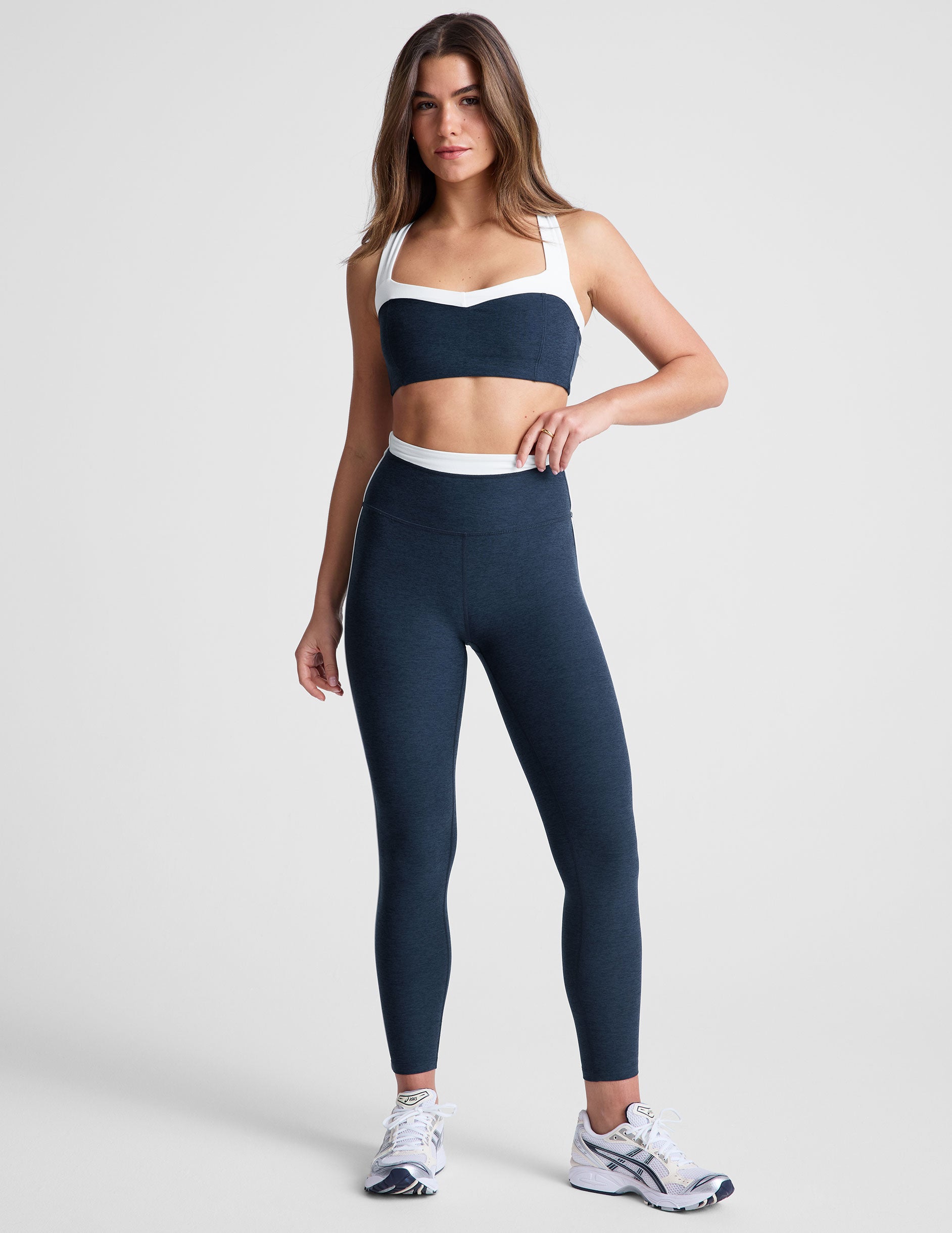 navy blue self-lined, medium to low support bra top with a colorblock sweetheart neckline panel, contrast straps, and princess seams. bra is paired with navy blue high-waisted midi leggings with a white contrast trim around waistband and down sides of legs.