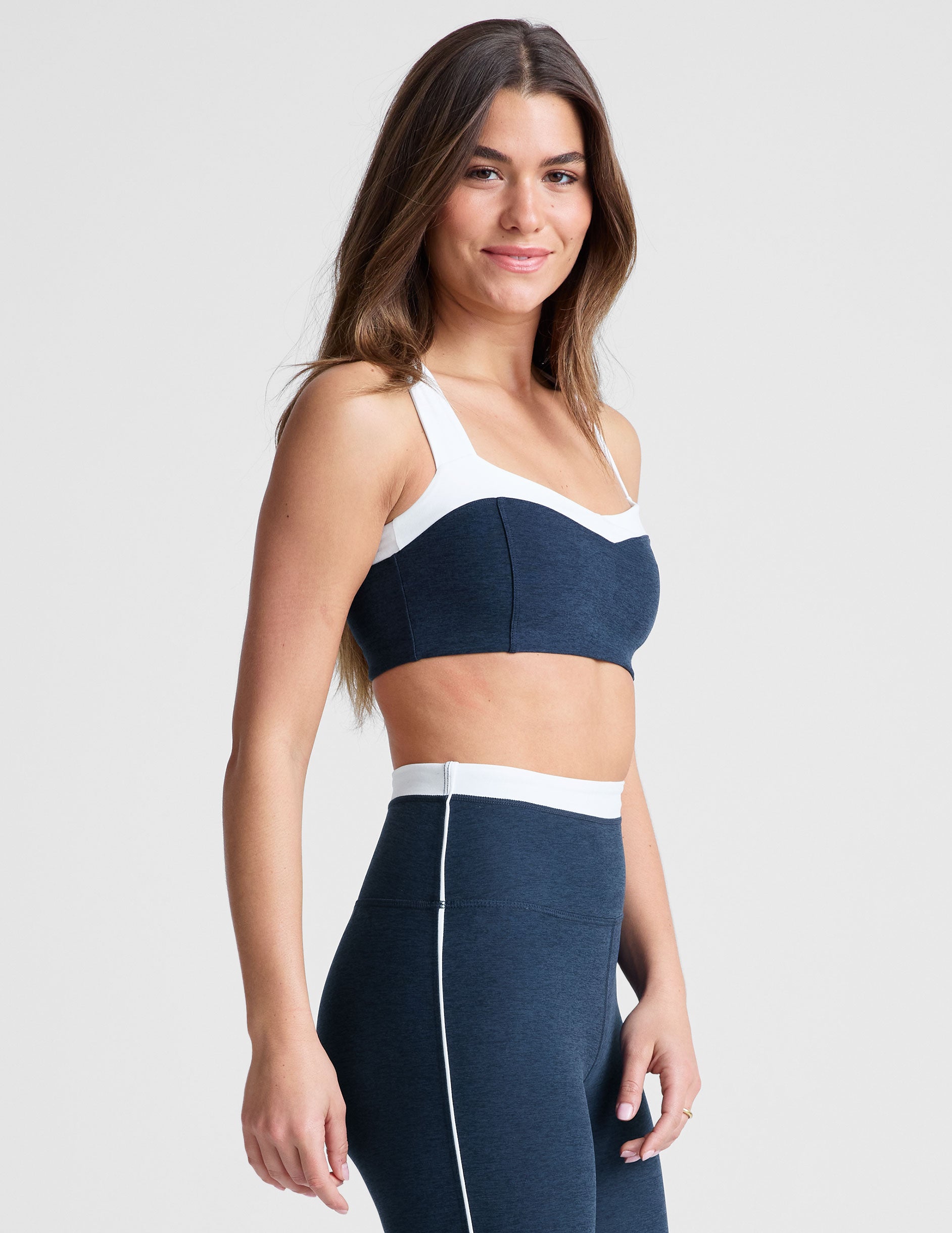 side view of navy blue self-lined, medium to low support bra top with a colorblock sweetheart neckline panel, contrast straps, and princess seams. bra is paired with navy blue high-waisted midi leggings with a white contrast trim around waistband and down sides of legs.