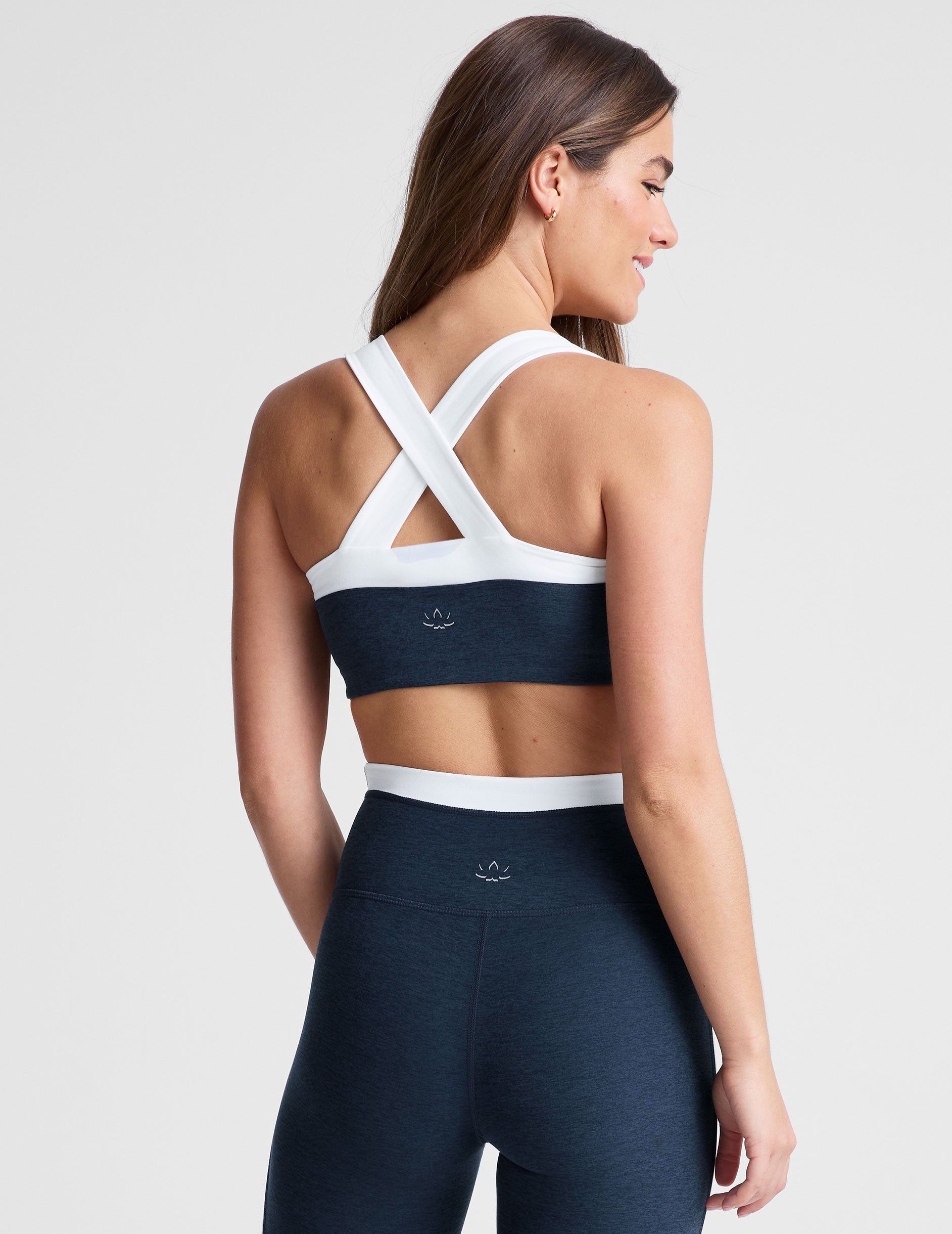 back view of navy blue self-lined, medium to low support bra top with a colorblock sweetheart neckline panel, contrast straps, and princess seams. bra is paired with navy blue high-waisted midi leggings with a white contrast trim around waistband and down sides of legs.