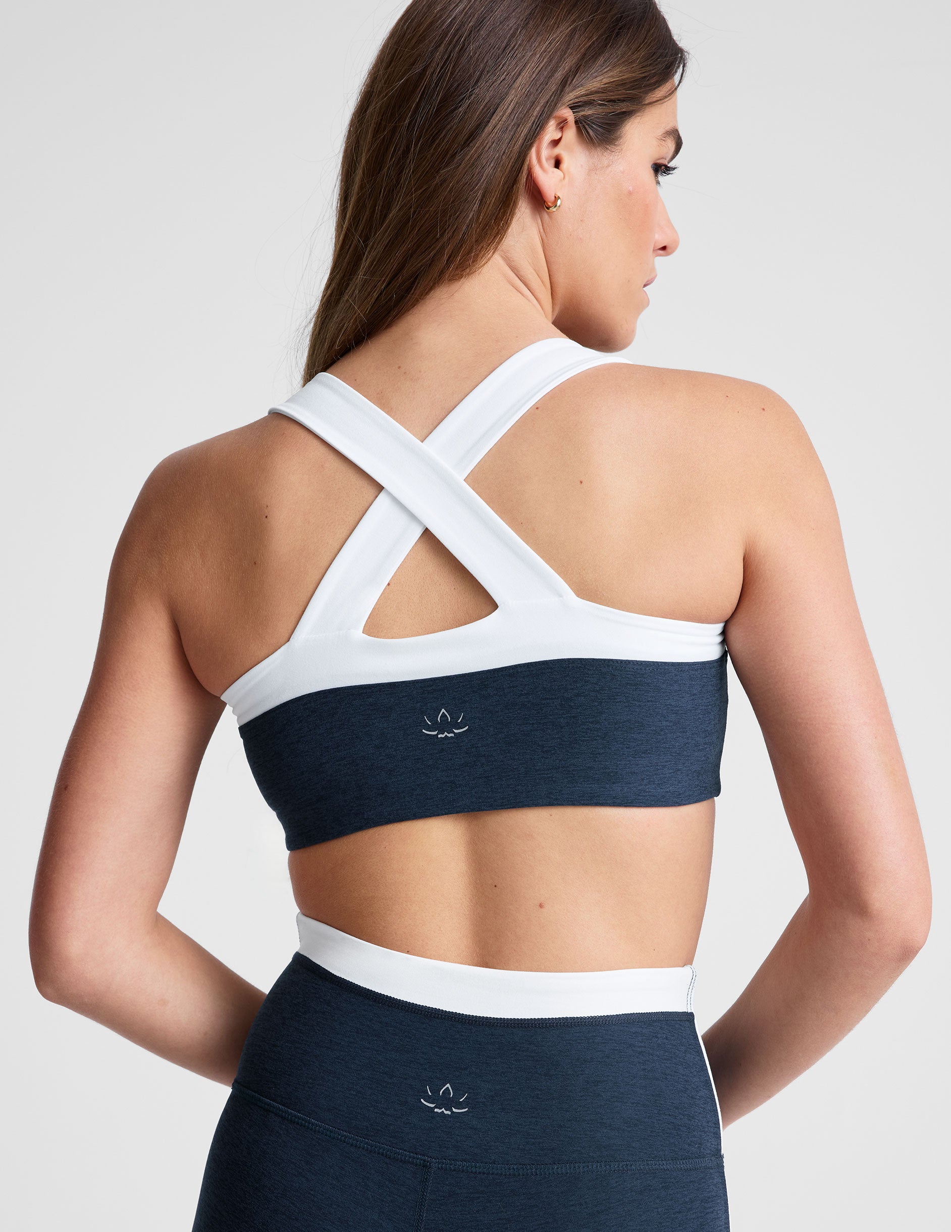 back view of navy blue self-lined, medium to low support bra top with a colorblock sweetheart neckline panel, contrast straps, and princess seams. bra is paired with navy blue high-waisted midi leggings with a white contrast trim around waistband and down sides of legs.