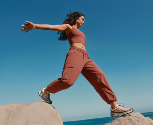 Woman in brown outfit standing on rocks with a clear blue sky and ocean background