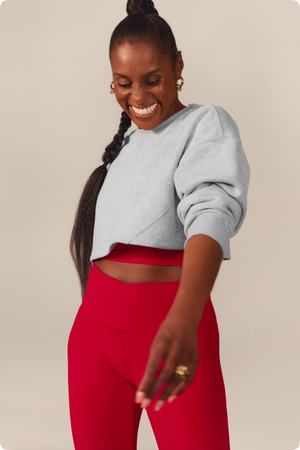 Issa Rae smiling and wearing a grey cropped sweatshirt and red pair of leggings.