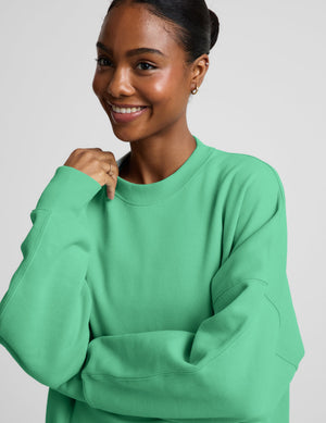 Woman wearing a green oversized crewneck sweatshirt and green leggings against a plain background. 