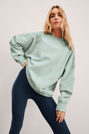 Woman wearing a light blue oversized sweatshirt and blue midi length jumpsuit. 