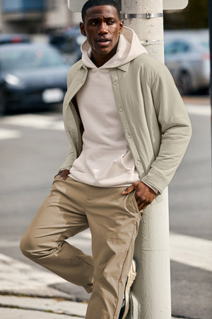 beyond yoga men's collection - male model wearing a white hoodie and brown chino pants. 