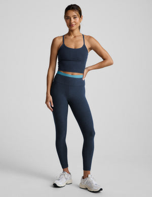 woman wearing a blue cropped tank top and navy blue layered midi leggings against a plain background. 