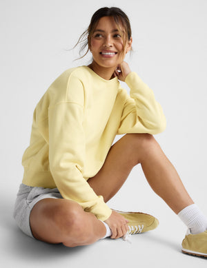 Woman wearing a yellow crew neck sweatshirt and grey sweat shorts. 