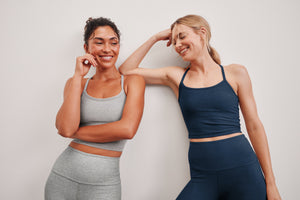 woman wearing a gray cropped tank and leggings posing with a woman wearing a navy blue cropped tank and leggings against a plain background. 