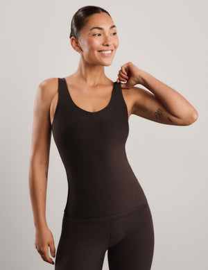 A woman modeling a dark brown v-neck tank top and matching leggings against a light gray studio background.