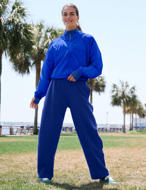 Woman wearing a green strappy bra and sweatpants against a plain background. 