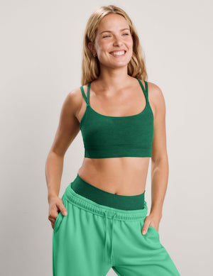 Woman wearing a green strappy bra and sweatpants against a plain background. 