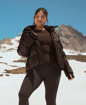 woman is wearing a brown puffer jacket and a brown long sleeve top and leggings. 