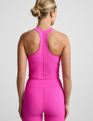 Woman wearing a bright pink ribbed cropped tank top and ribbed biker shorts against a plain background. 