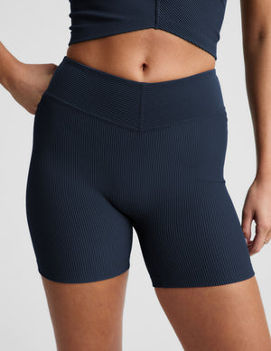 Woman wearing a navy blue ribbed cropped tank and biker shorts against a plain background. 