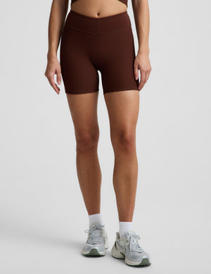 Woman in a brown ribbed cropped tank and brown ribbed biker shorts against a plain background. 