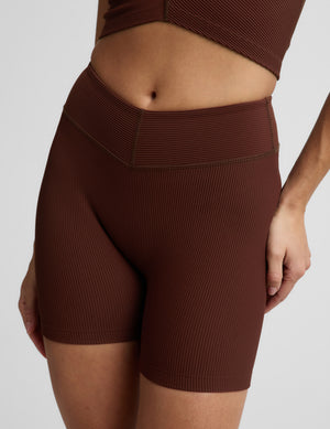 Woman in a brown ribbed cropped tank and brown ribbed biker shorts against a plain background. 