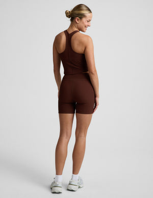 Woman in a brown ribbed cropped tank and brown ribbed biker shorts against a plain background. 