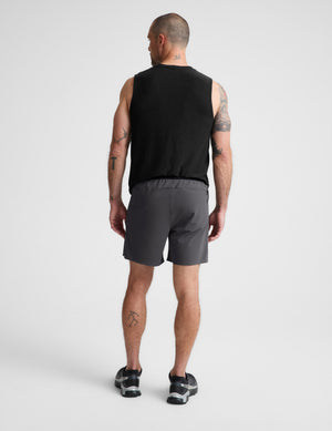 Man wearing a black sleeveless shirt and gray shorts on a plain background. 