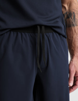Man wearing a navy sleeveless shirt and shorts on a white background. 