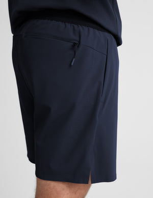 Man wearing a navy sleeveless shirt and shorts on a white background. 