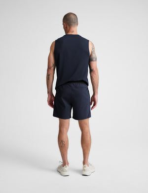 Man wearing a navy sleeveless shirt and shorts on a white background. 