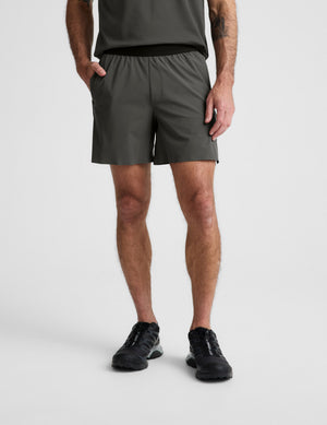 Man wearing a dark green t-shirt and shorts set on a light gray background. 