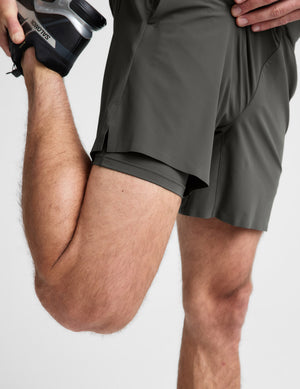 Man wearing a dark green t-shirt and shorts set on a light gray background. 